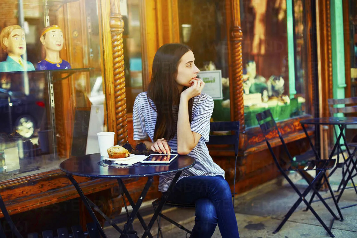 thoughtful woman sitting by table at sidewalk cafe on sunny day