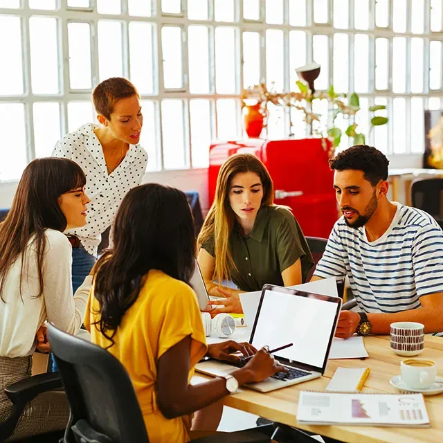 Tiga rekan kerja berdiskusi fokus di depan laptop.